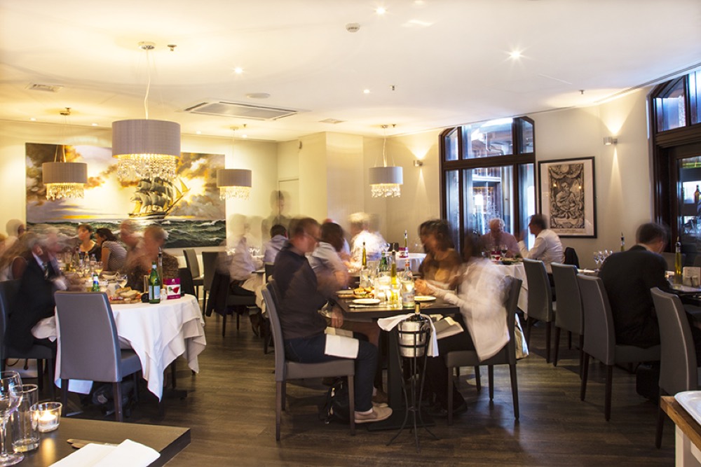 The dining room at Amerigo Vespucci, warmly lit with chandeliers and a large painting of the tall ship on the wall
