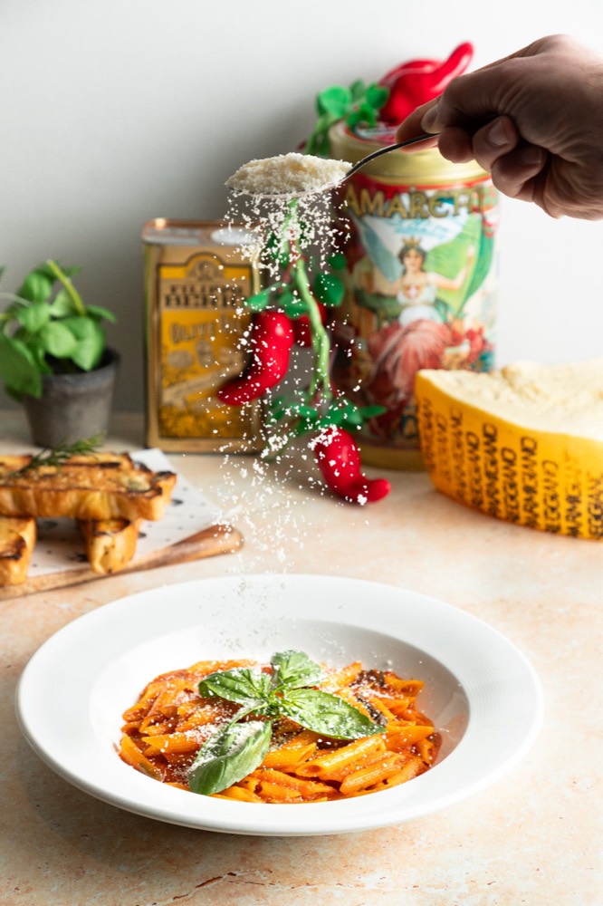 Penne in tomato sauce with grated parmesan falling from a spoon and fresh basil