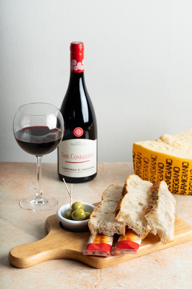 Bottle of Italian red wine with a poured glass, parmesan and a board of bread and olives