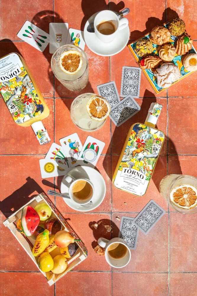 Flat lay of limoncello, espresso cups, Sicilian playing cards and fruit on terracotta tiles