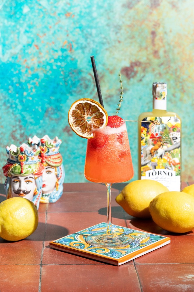 Strawberry cocktail garnished with dried orange, beside lemons and a Sicilian ceramic